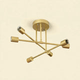 Gold-colored iron sputnik chandelier with six cylindrical sockets on crossing arms against a cream background.