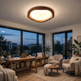 A modern oval ceiling light with a warm wood frame and glowing white glass, mounted on the ceiling of a contemporary living room with large windows, armchairs, and a wooden desk.