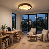 A modern circular ceiling light with a warm glowing LED light and a dark wood frame, installed in a contemporary, well-lit living room with wooden floors, chairs, and a desk.