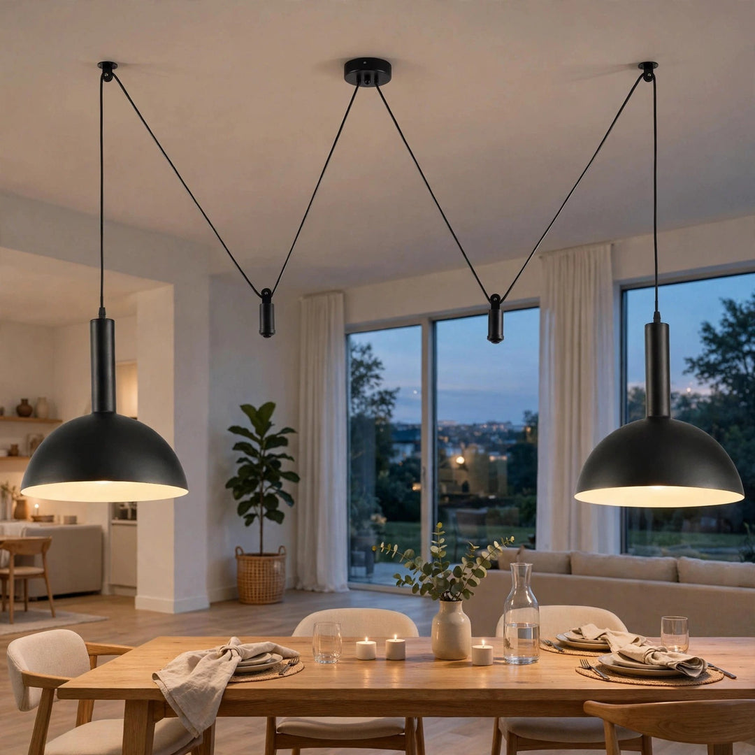 Two black dome pendant lights hanging over a dining table in a modern, well-lit living space with large windows and a view of the city at dusk.
