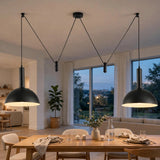 Two black dome pendant lights hanging over a dining table in a modern, well-lit living space with large windows and a view of the city at dusk.