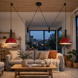 A modern living room with two red dome pendant lights hanging from black cords above a beige sofa, with a wooden coffee table and large windows in the background.