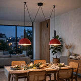 Two red dome pendant lights hanging over a wooden dining table in a modern, warmly lit dining room.