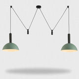 A modern two-light pendant ceiling fixture with sage green dome shades and black cords, suspended against a light gray background.