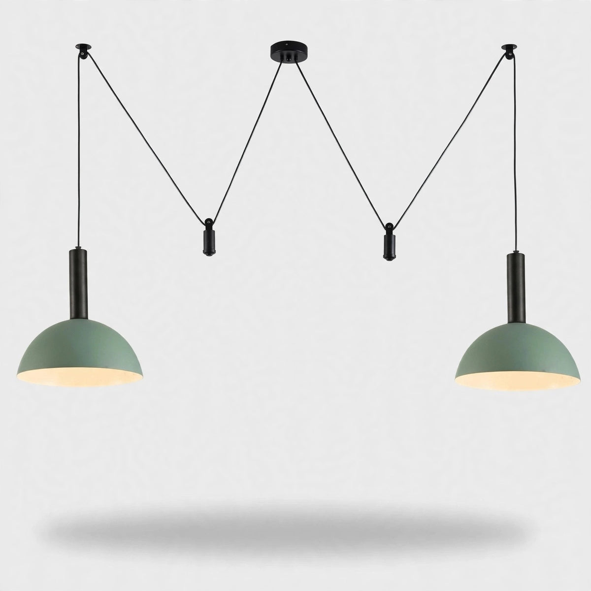 A modern two-light pendant ceiling fixture with sage green dome shades and black cords, suspended against a light gray background.