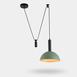 A modern pendant light with a muted sage green dome shade and a black cord suspension system, shown against a light gray background.