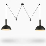 A modern two-light pendant ceiling fixture with matte black metal dome shades and warm white light, suspended by thin cords from a central ceiling mount against a white background.