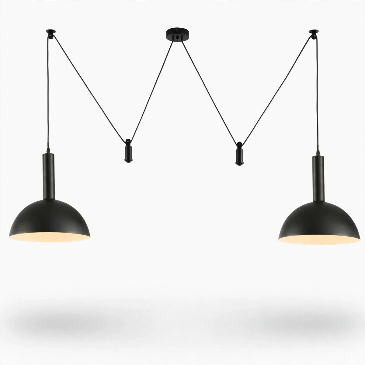 A modern two-light pendant ceiling fixture with matte black metal dome shades and warm white light, suspended by thin cords from a central ceiling mount against a white background.