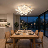 A modern white lotus-shaped ceiling light fixture illuminates a dining room with a wooden table, woven-back chairs, and large floor-to-ceiling windows overlooking a city skyline at dusk.