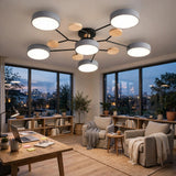 A modern multi-light ceiling fixture with six circular gray shades and light wood accents, mounted on a black central hub. The fixture is shown installed in a contemporary living room with large windows, a wooden desk, and two beige armchairs.