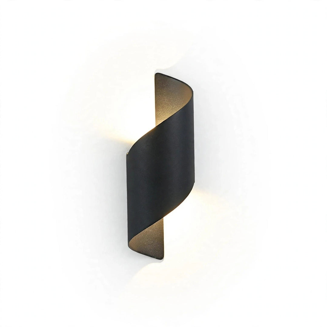 A modern spiral-shaped wall sconce in a matte black finish, emitting a warm glow against a clean white background.