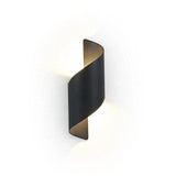 A modern spiral-shaped wall sconce in a matte black finish, emitting a warm glow against a clean white background.
