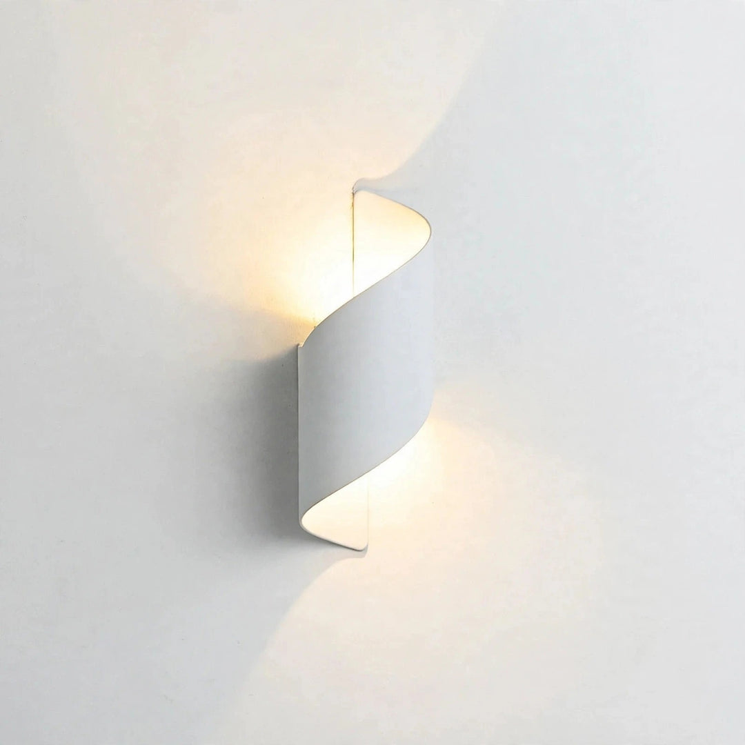 A modern spiral-shaped wall sconce light fixture in a matte white finish, emitting a warm yellow glow against a clean white wall.