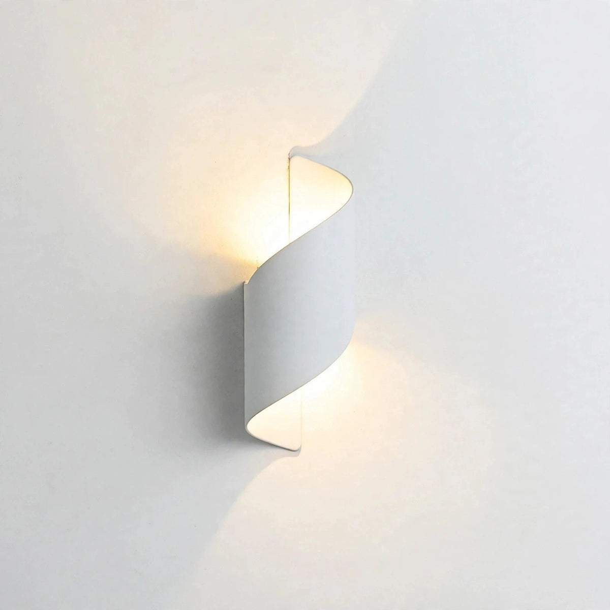 A modern spiral-shaped wall sconce light fixture in a matte white finish, emitting a warm yellow glow against a clean white wall.