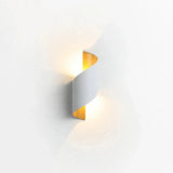 A modern spiral-shaped wall sconce with a white outer body and a warm yellow-gold inner panel, shown illuminated against a plain white wall.