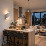 White spiral aluminum wall sconce casts warm light beside a kitchen island in an open-plan living space.