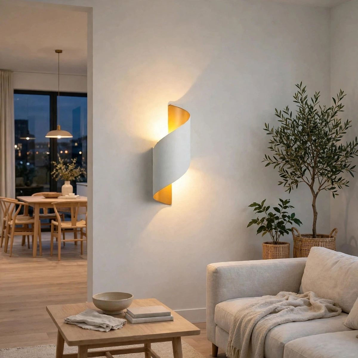 A modern spiral-shaped wall sconce with a white outer shell and a warm gold inner accent, emitting a soft glow on a light beige wall in a contemporary living room setting.