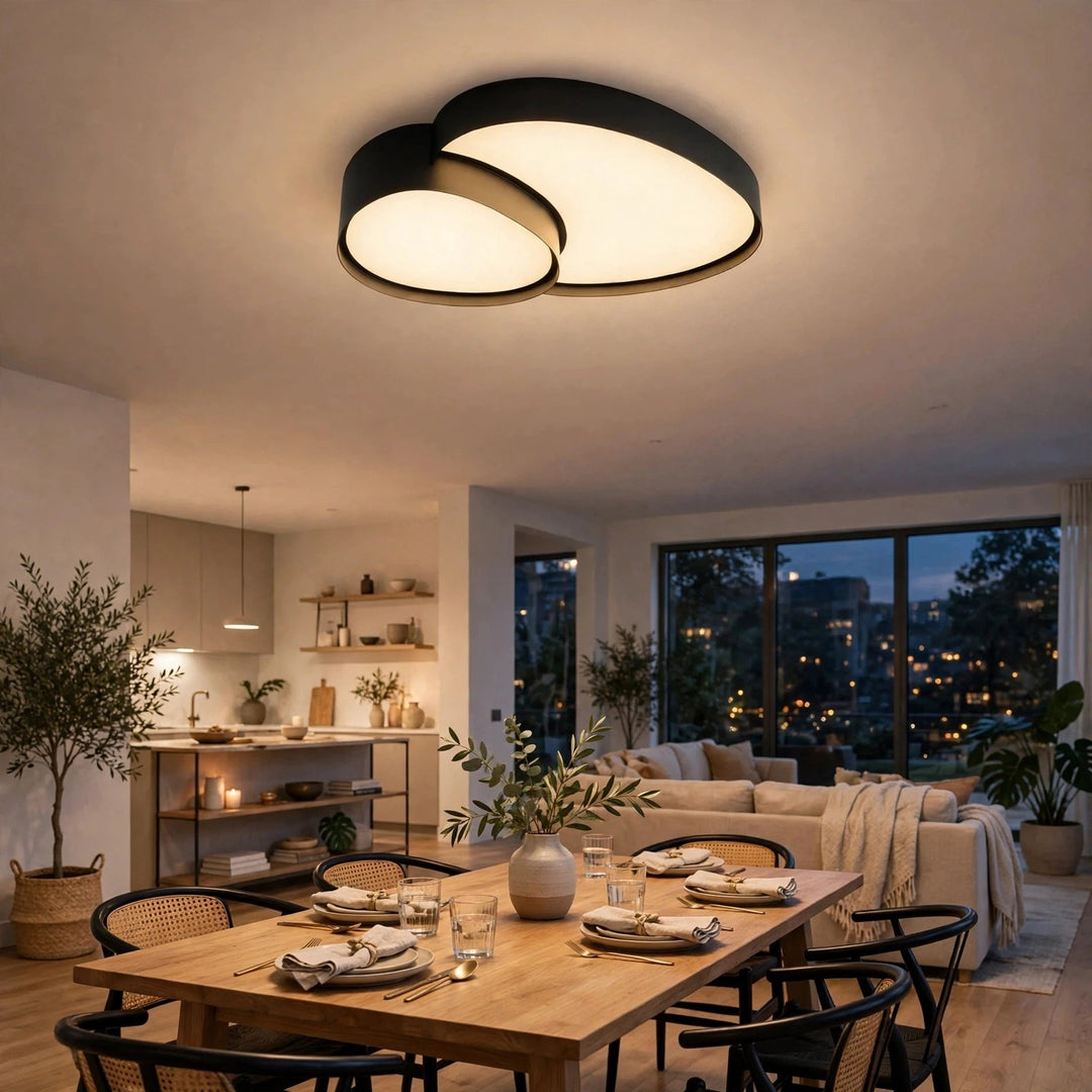 A modern two-light cluster ceiling fixture with black metal frames and warm white glowing diffusers, installed in a contemporary dining room above a wooden table set for dinner.