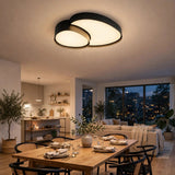 A modern two-light cluster ceiling fixture with black metal frames and warm white glowing diffusers, installed in a contemporary dining room above a wooden table set for dinner.