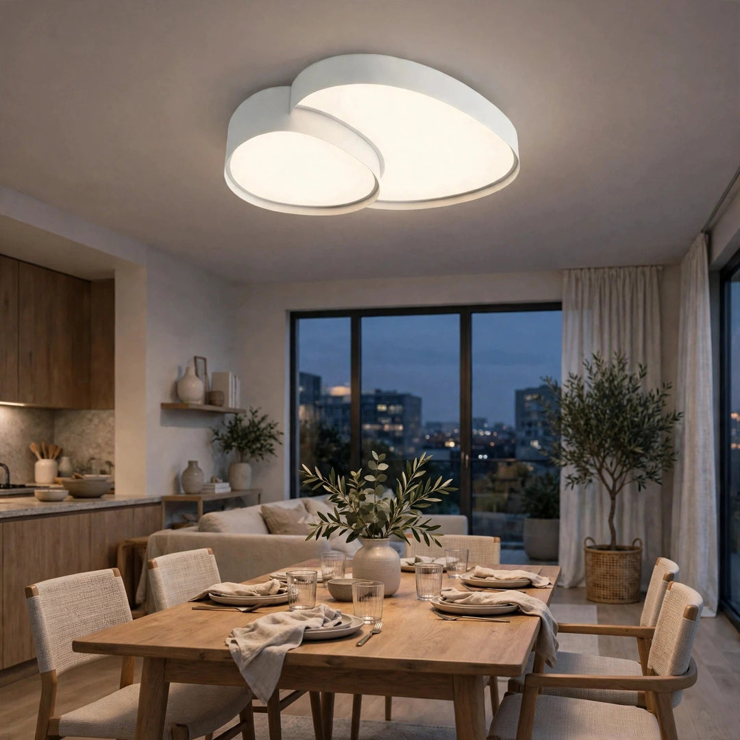 A modern double-ring LED ceiling light fixture with a white finish, glowing in a contemporary dining room setting with a wooden dining table and chairs.