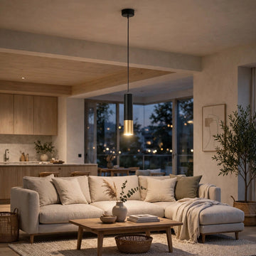 A modern black pendant light with a brushed gold cylindrical diffuser hangs over a beige sectional sofa in a warm, contemporary living room.