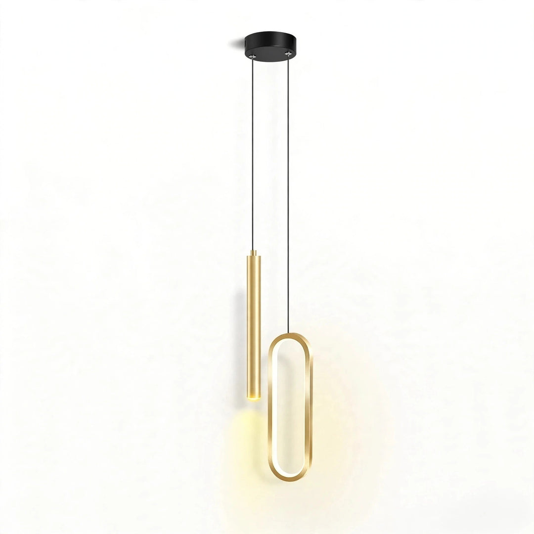 Modern pendant light fixture with a black circular ceiling mount, two slim black suspension cords, one gold cylindrical shade, and one elongated gold oval frame, shown against a plain white wall with warm light glow.