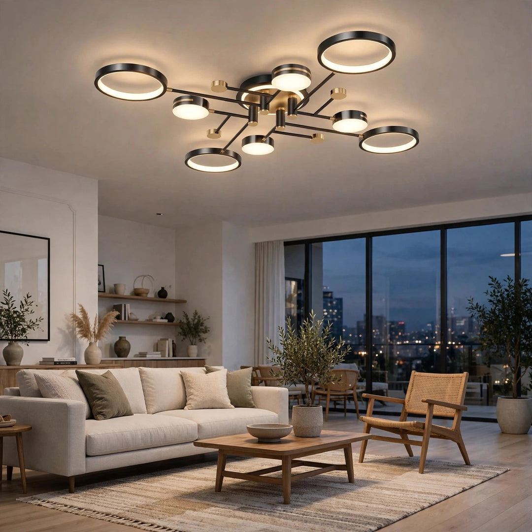 Modern multi-light ceiling fixture with circular LED rings and a brushed brass center, installed in a contemporary living room with a sofa, coffee table, and large windows overlooking a city skyline at dusk.