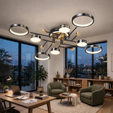 A black ceiling light with circular rings and gold accents glows above a home office with green armchairs and a wooden desk.