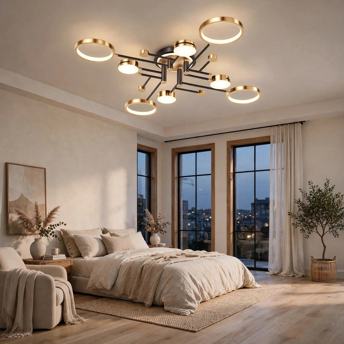 Gold and black ceiling light with circular illuminated discs above a cream bed beside tall windows and a potted tree.