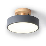 A modern semi-flush mount ceiling light fixture featuring a matte dark gray cylindrical shade, a natural light wood ceiling mount, and a glowing white diffuser, shown against a plain white background.