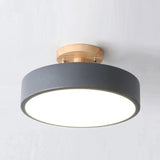 A modern semi-flush mount ceiling light with a matte dark gray cylindrical shade, a natural wood ceiling canopy, and a bright white diffuser, shown against a plain light gray wall.