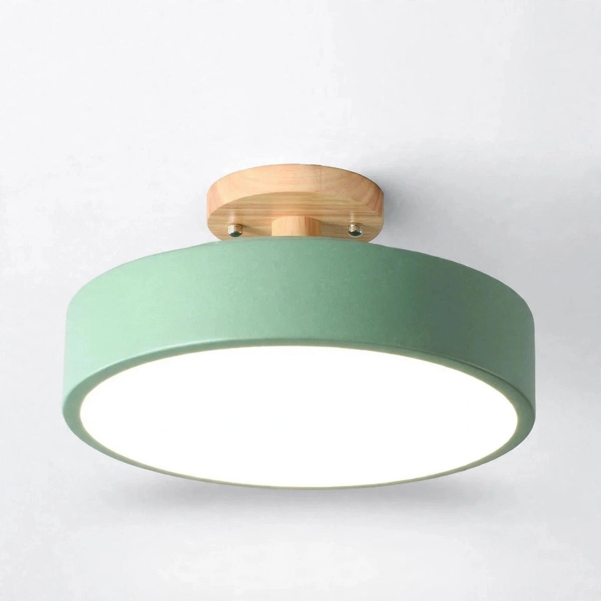 A modern semi-flush mount ceiling light with a matte sage green cylindrical shade, a natural wood ceiling mount, and a bright white diffuser, shown against a plain white wall.