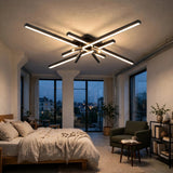 Black crossed linear-bar ceiling light with spotlights glowing above a bed in a bedroom with large windows at dusk.