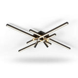 Black crossed linear-bar ceiling light with warm glowing bars and spotlights, seen from slightly below on a white background.