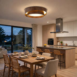 A modern circular ceiling light with a dark wood frame and warm glowing LED light, installed in a contemporary dining and kitchen room.