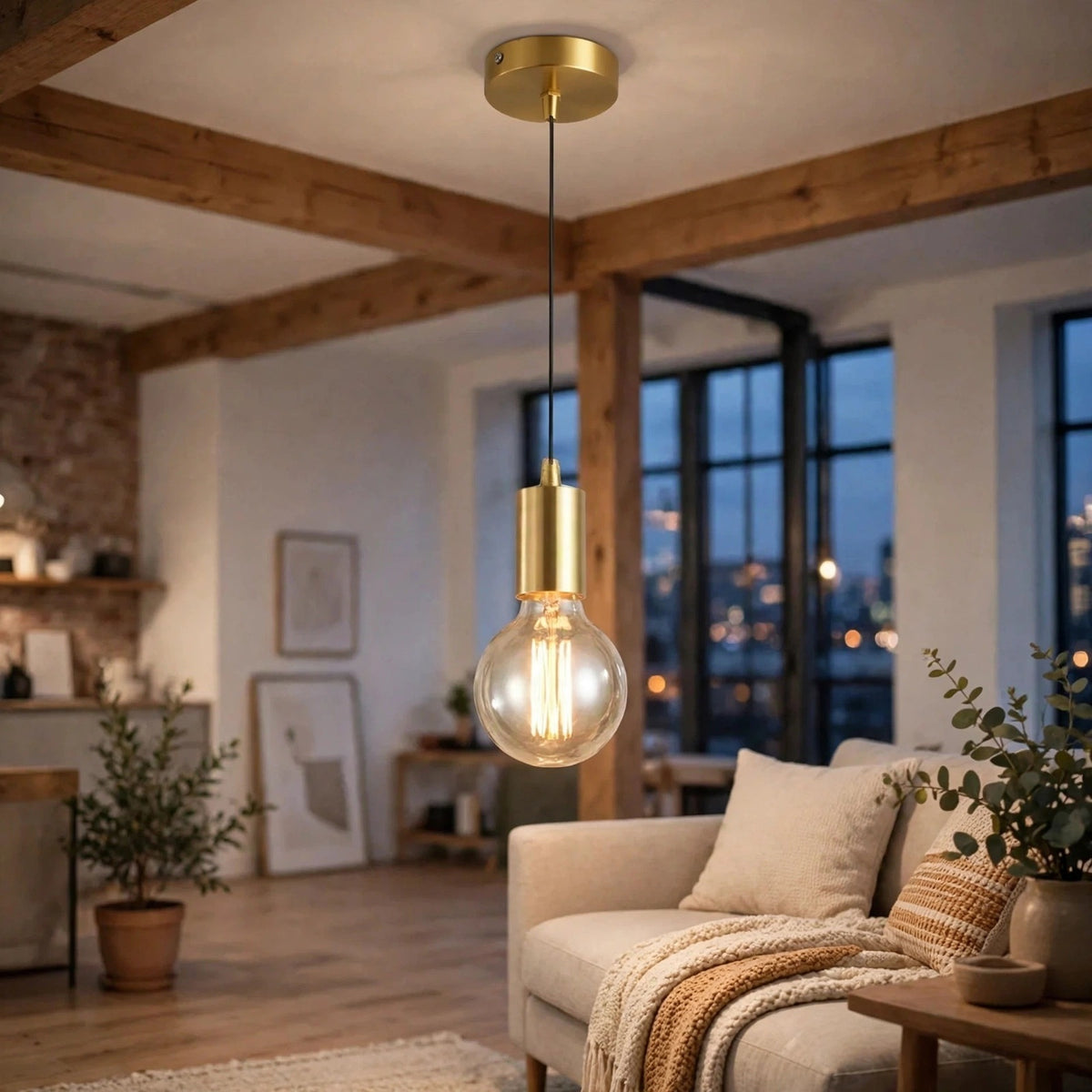 A modern brass pendant light with a clear glass bulb hangs in a cozy living room with wooden ceiling beams, a beige sofa, and warm ambient lighting.
