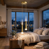 A modern bedroom interior with a bed dressed in cream bedding, large windows with white curtains, and a brass ceiling pendant light casting light onto the floor and bedding.