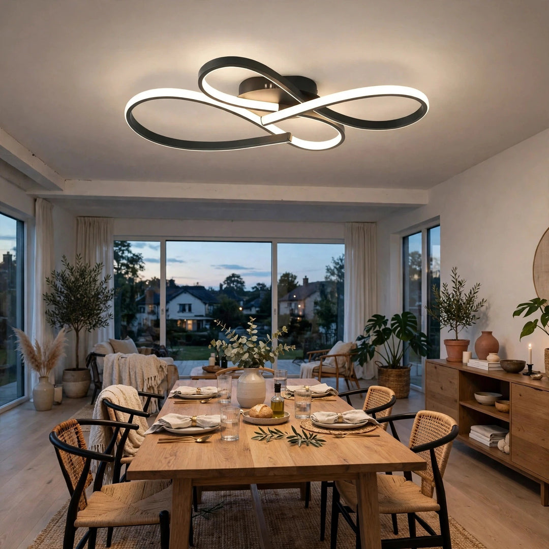 Modern black metal infinity loop ceiling light with a white illuminated diffuser, mounted on the ceiling of a contemporary dining room with a wooden dining table and chairs.