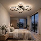 Modern multi-ring LED ceiling light fixture with a black frame and warm white glow, installed in a contemporary bedroom with large windows and neutral bedding.