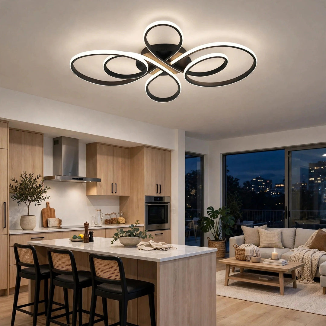 Modern ceiling light fixture with interlocking black and gold circular rings and a warm white LED glow, installed in a contemporary kitchen and living room setting.