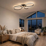 Modern ceiling light fixture with interlocking abstract oval rings in black and brushed silver, illuminated in a contemporary bedroom setting.