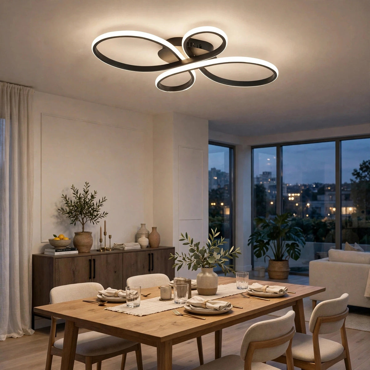 Modern LED ceiling light fixture with three interlocking circular rings in a black finish with white illuminated edging, shown installed in a contemporary dining room with a wooden table, chairs, and large windows overlooking a city view at dusk.