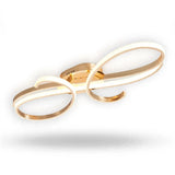 A gold ceiling light with overlapping curved bands and a reflective central mount is shown illuminated against a white background.