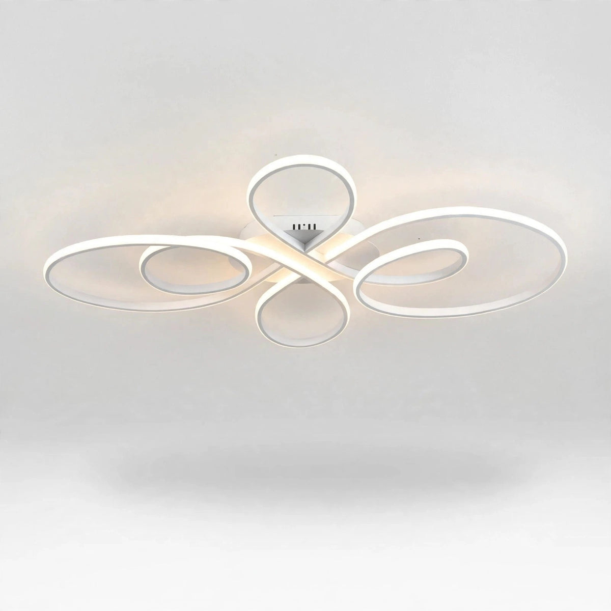 A modern ceiling light fixture with flowing, abstract oval loops in a glossy white finish, emitting a warm light glow against a clean white ceiling.