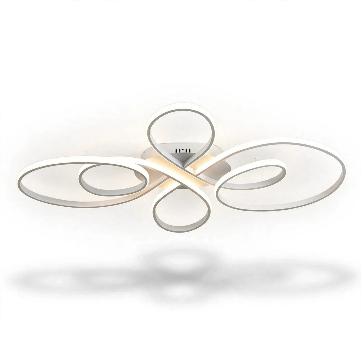 A modern ceiling light fixture with flowing, abstract oval loops in a brushed silver finish, emitting a warm white glow from its central LED light source, shown against a plain white background with a soft shadow below.