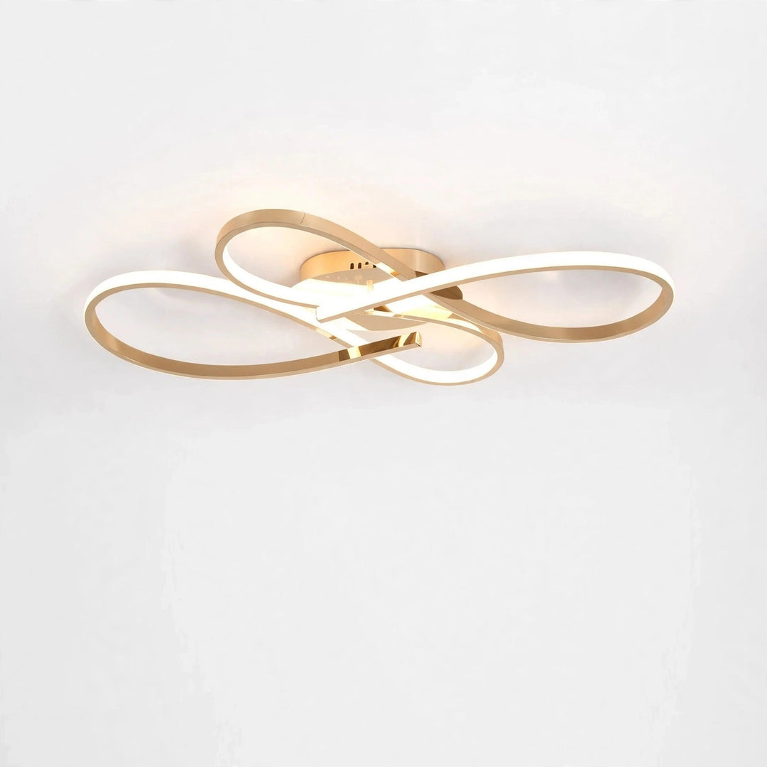 Modern ceiling light fixture with interlocking gold and white LED loops, shown mounted against a plain white wall.