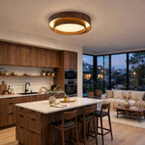 A modern circular ceiling light with a dark wood frame and warm glowing LED, installed in a contemporary kitchen and living room setting.