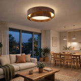 A brown woodgrain flush mount light with illuminated circular rings sits above a cream sofa in an open living and dining room.