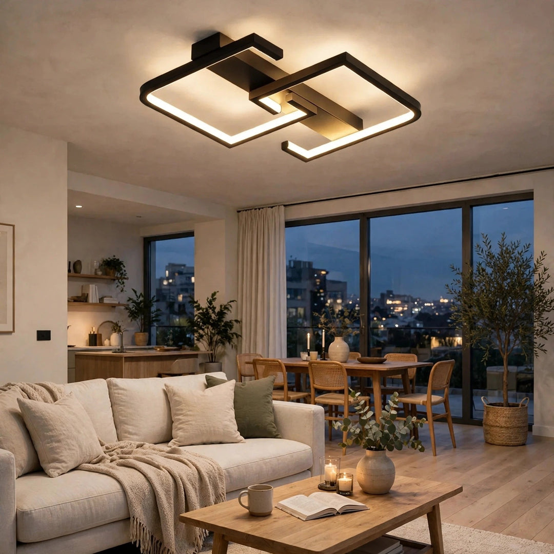 Modern geometric LED ceiling light fixture with a black and bronze frame, glowing in a contemporary living room with a sofa, coffee table, and large windows overlooking a city skyline at dusk.