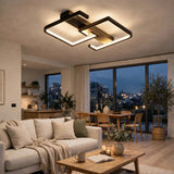 Modern geometric LED ceiling light fixture with a black and bronze frame, glowing in a contemporary living room with a sofa, coffee table, and large windows overlooking a city skyline at dusk.